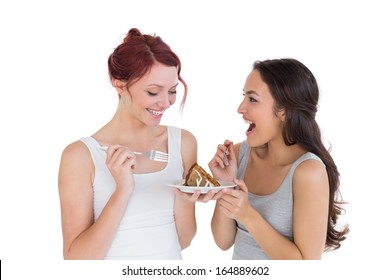 Two cheerful young female friends eating pastry together over white background