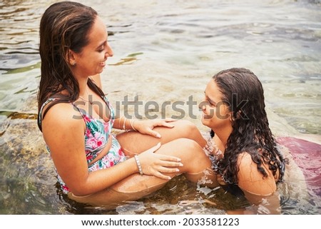 Two cheerful young women laughing in a natural pool in beach
