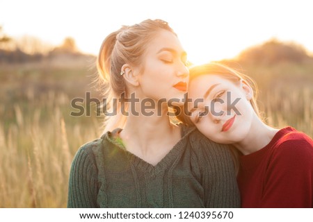 Two cheerful young women standing on the field at sunset.Best friends