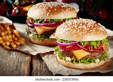 Two cheeseburgers on sesame buns with succulent beef patties and fresh salad ingredients served with French Fries on crumpled brown paper on a rustic wood table - Powered by Shutterstock