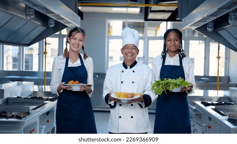 Two chef's assistants holding a bowl of pasta ingredients, walking slowly in the kitchen with a smile. before pointing to the chef presenting the ingredients that have been prepared - Powered by Shutterstock