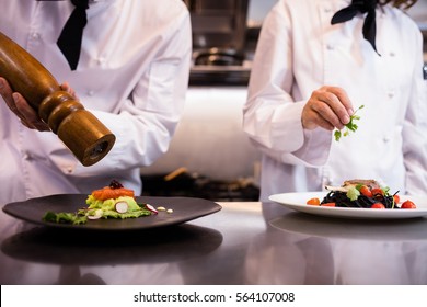 Two chefs garnishing meal on counter in commercial kitchen - Shutterstock ID 564107008