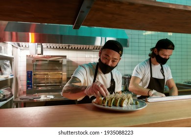 Two chefs preparing delicious sushi in a restaurant. Middle-aged chef sprinkling sushi with seeds. Healthy and tasty food in the restaurant kitchen. Healthy food from the sea concept