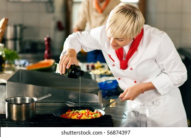 Two chefs in teamwork - man and woman - in a restaurant or hotel kitchen cooking delicious food, she is putting olive oil in the ratatouille