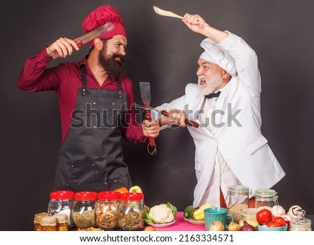 Two chefs in uniform fighting with kitchen utensils. Cooking. Culinary battle. Competition of chef.