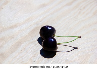 Two cherries as a pair with strings places on a wooden surface, with a shadow
