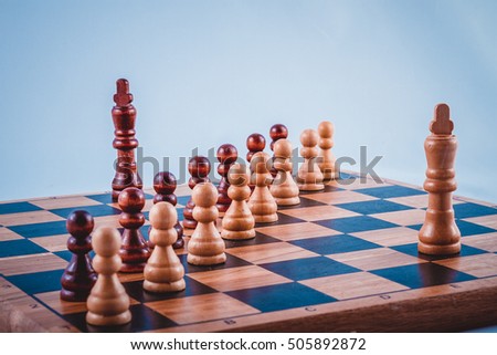 Two chess king on a Board separated by two rows of pawns, wooden chess pieces on the Board, White and black pawns are in two rows, retro photo
