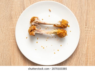 Two Chicken Bones As Left Over On White Plate. Unhealthy Fast Food, Chicken Legs, Top View