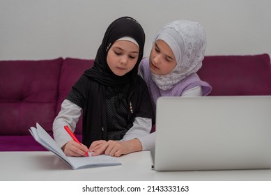 Two Child Girls In The Hijab Together Learn For School At The Home Desk. Sister Helping Little Sister To Do Homework. Young Muslim Students Have Online Education.