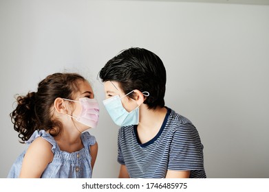 Two Child Playing With Mask In Coronavirus Times. Brothers Trying To Put On A Surgical Mask To Go Outside In The Confinement Due To The Coronavirus. Social Distancing Measures To Avoid Contagion