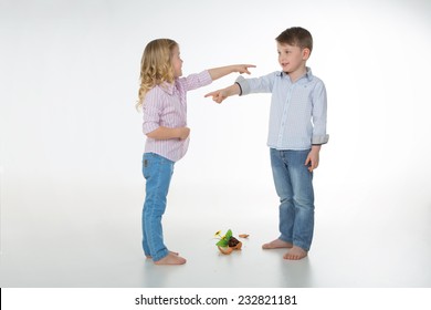 two children blaming each other for a fallen vase of flowers