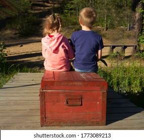 two children, a boy and a girl with blond hair, are sitting on a wooden box, in the woods, with their backs. Summer, evening, children in the forest. Love, caring, brother and sister in nature.World 