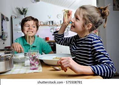 Two Children, Brother And Sister, Are Being Silly While Eating Spaghetti At Home In Their Kitchen