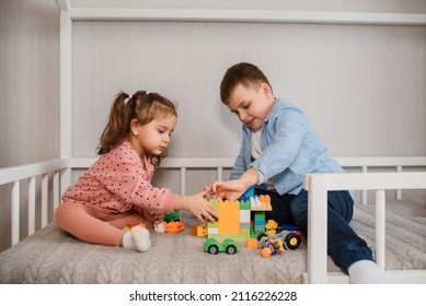 Two Children Brother And Sister Are Sitting In A Montessori Bed And Playing With Toy Bricks Cube. Bed For Kids In A House Shape.