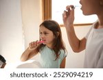 Two children brush their teeth in a sunlit bathroom, promoting healthy dental habits and hygiene routines.