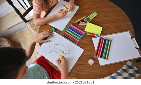 Two children drawing with colorful pencils at a wooden table, fostering creativity and artistic expression in a home environment. - Powered by Shutterstock