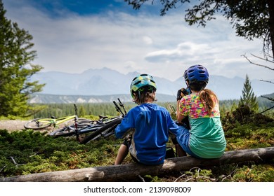 Two children eating a snack while taking a break on a mountain biking trip overlooking a mountain valley in Banff National Park Canada.