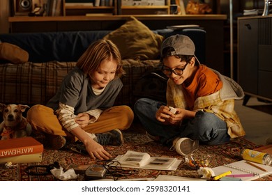 Two children engaging with gadgets while sitting on floor in cozy room, having relaxed expressions and displaying curiosity about the technology around them