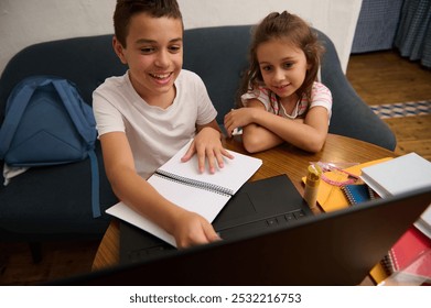 Two children engaging in online learning at home. They are smiling while using a laptop and notebooks, fostering a productive study environment. - Powered by Shutterstock