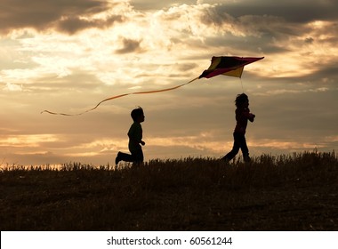 Two children enjoy flying a kite during sunset. - Powered by Shutterstock