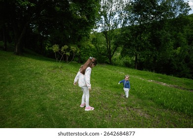 Two children exploring grassy fields surrounded by tall trees on a sunny day.
