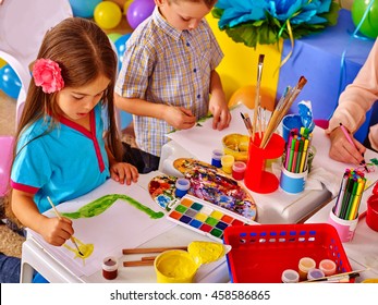 Two Children Girl And Boy With Brush Painting On Table In Primary School. Painting Children Lesson In Primary School. Small Table In Painting Class.