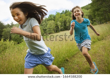 Two children, girls running and playing chase, laughing in the fresh air.
