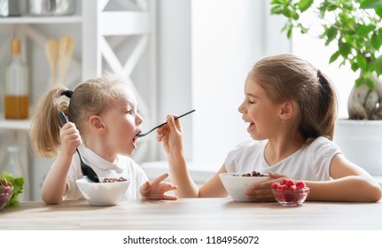 Two Children Having Breakfast. Kids Eating Cereal And Berry In Kitchen.