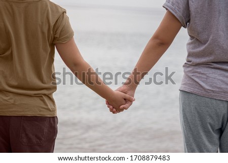 Two children hold hands in front of the sea on the beach, during a cloudy day. Concept of company facing the unknown.