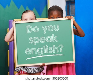 Two children holding a chalkboard saying "Do you speak english?" in preschool