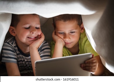 Two children holding digital tablet under blanket - Powered by Shutterstock