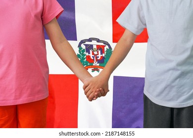 Two Children Joined Hands On Flag Dominican Republic Background. Boy And Girl Joined Hands On Background Flag Of Dominican Republic. Concept Of Family And Parenting In Dominican Republic