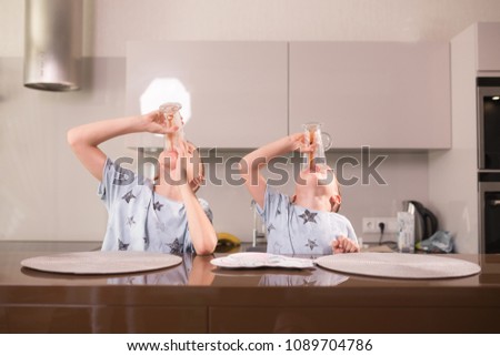 Two children in the kitchen drink hot chocolate from glasses.