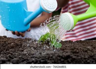 Two children little girl watering young tree with watering pot together - Powered by Shutterstock