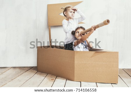 Two children little girls home in a cardboard ship play captains and sailors