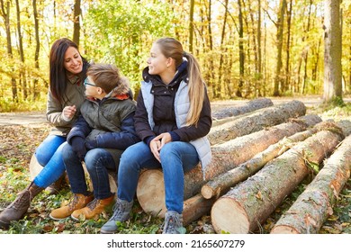 Two Children And A Mother Sit Relaxed On Tree Trunks During An Excursion In Nature In The Forest