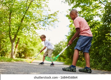 Two children play hockey on a street in summer