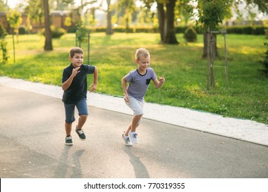 Two Children Are Playing In The Park. Two Beautiful Boys In T-shirts And Shorts Have Fun Smiling. They Eat Ice Cream, Jump, Run. Summer Is Sunny