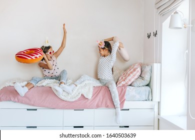 Two Children Playing Together In Bed, Having Fun In Bright Girly Playroom. Kids Paljamas Party In White Bedroom Interior.