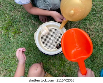 Two Children Playing Toys Together. One Kid Poured Water From A Plastic Teapot Into A Plastic Strainer