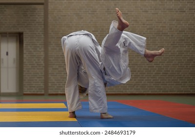 Two children practising judo martial arts. Indoors. Boy throws another kid. Fighting in white uniforms.  - Powered by Shutterstock