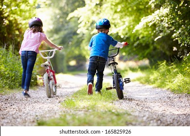Two Children Pushing Bikes Along Country Track