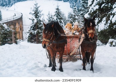 Two children ride on a retro sleigh with horses in winter time. Mountain snowy landscape background. Tours, horse riding. - Powered by Shutterstock