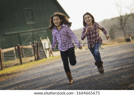 Two children running along a road, by a farm building, on an organic farm.