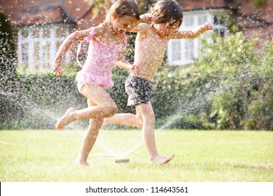 Two Children Running Through Garden Sprinkler