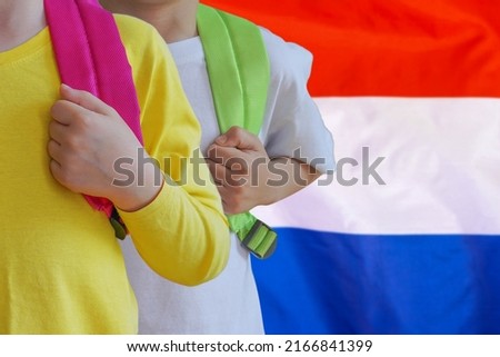 Two children with satchels background of Netherlands flag. Concept of upbringing and educating children in Dutch