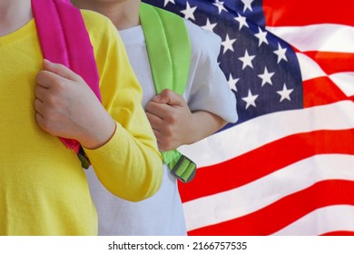 Two Children With Satchels Background Of US Flag. Concept Of Upbringing And Educating Children In USA