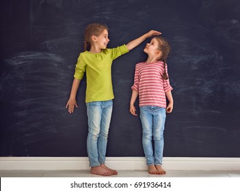 Two children sisters play together. Kid measures the growth on the background of blackboard. Concept of education.
