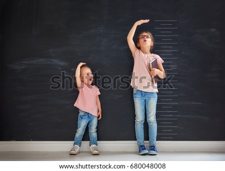 Two children sisters play together. Kid measures the growth on the background of blackboard. Concept of education.