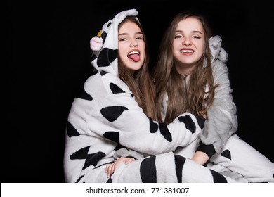 Two Children, Sisters Are Wearing Animal Pajamas. Merry Christmas And Happy Holidays Concept. Family Holiday, Party Over Black Background. Cute Teenage Sisters. Halloween Concept.  